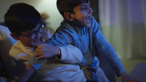 Two-Young-Boys-At-Home-Having-Fun-Playing-With-Computer-Games-Console-On-TV-Fighting-Over-Controllers-Late-At-Night